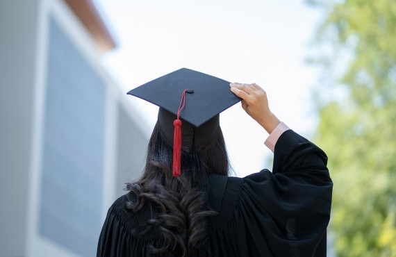 Photo shows the back of a woman's head. She has long dark hair and is wearing a graduation cap.