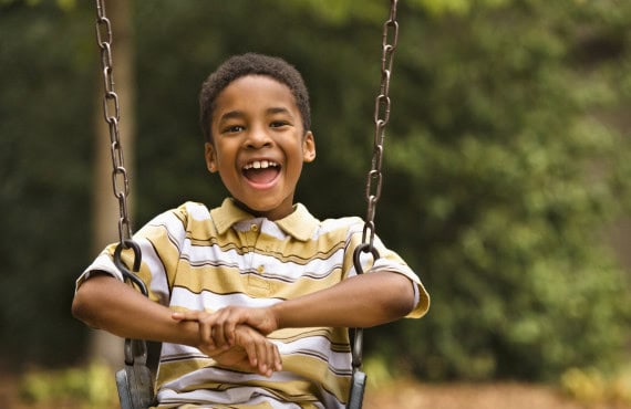 A young boy smiling while sitting on a swing.