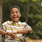 A young boy smiling on a swingset.