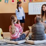 A group of three children sitting and listening to another student present the alphabet.