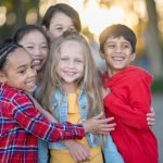 A group of five children smiling and hugging.